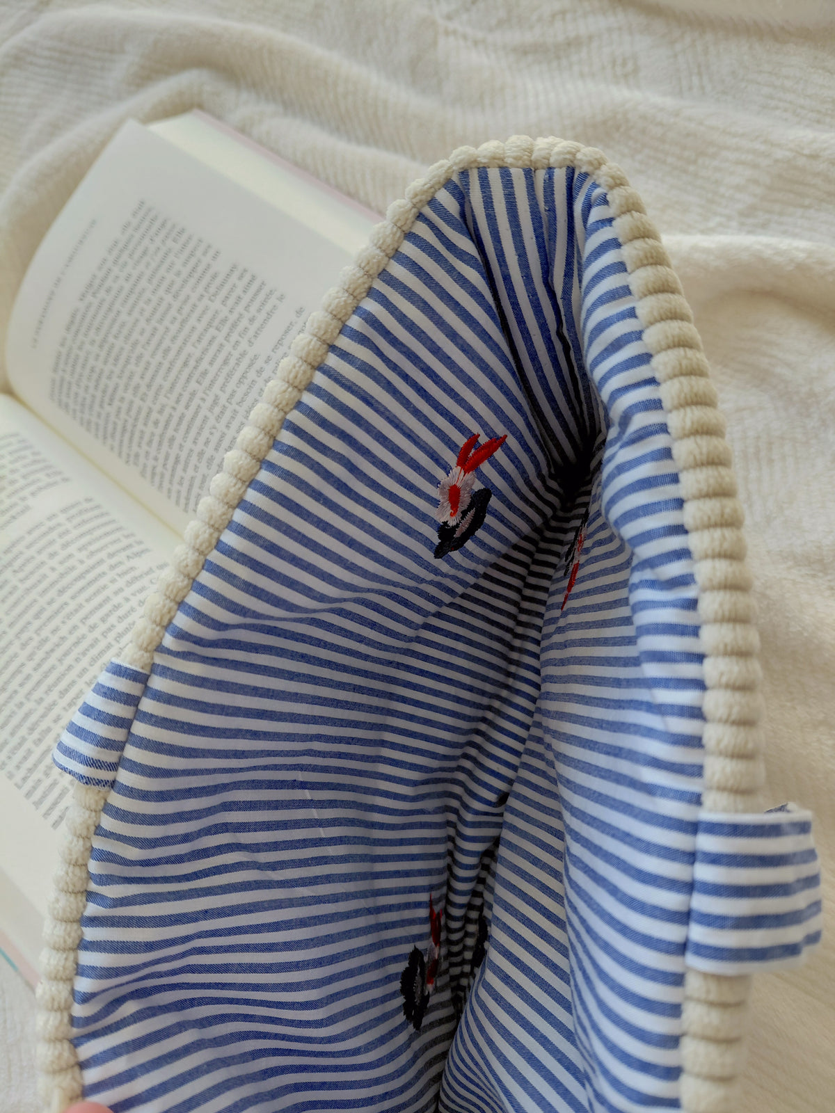 Pochette à livre format broché en velours. Zoom sur l'intérieur qui est à rayures blans et bleu avec fleurs brodées